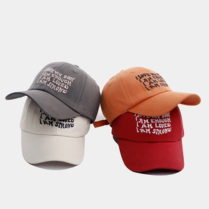 Detail of four baseball caps in grey, orange, beige, and red with embroidered quotes