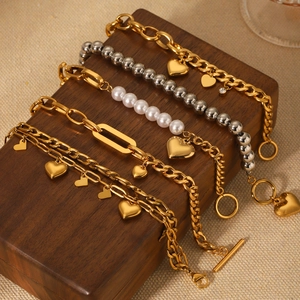 Gold and silver layered pearl bracelets with heart pendants on a wooden box