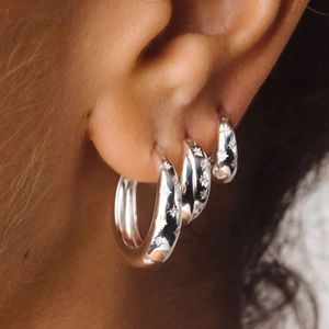 Detailed close-up of layered S925 sterling silver star engraved hoop earrings on model ear