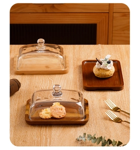 Detail of rectangular acacia wood butter dishes with clear glass lids on a wooden table