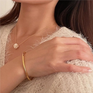 Close-up of a delicate pearl cluster necklace and a sleek gold bangle on a model