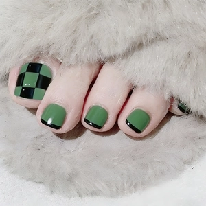 Detail of green and black checkered press-on toenails on soft grey plush background