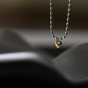 Macro detail of polished gold heart pendant on a silver-tone beaded chain necklace