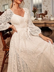 Détail d'une robe en dentelle blanche avec boutons col en V et nœud en satin à la taille