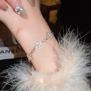 Detailansicht eines goldenen Kleeblatt-Armbands mit weißem Inlay und Zirkonia-Steinen