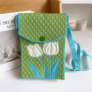 Detail of green knit phone bag featuring white tulip pattern and blue braided strap