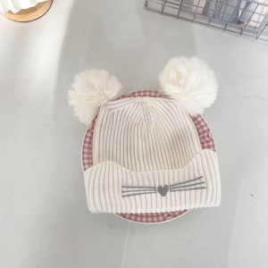 Close-up of winter knit hat featuring fluffy white double pom poms and cat embroidery