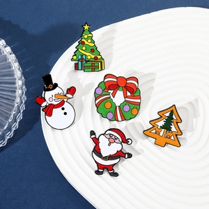 Set of five Christmas enamel pins with Santa and snowman designs on a ceramic plate