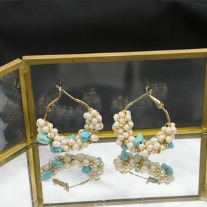 Macro shot of gold wire-wrapped earrings with white pearls and turquoise in a glass box