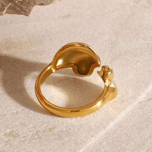 Detailed view of polished gold water drop ring with organic lines on beige stone