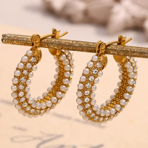 Close-up of gold hoop earrings with inlaid pearls and sparkling crystals on prop branch