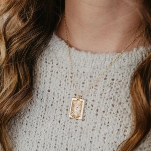 Close-up of golden tarot card pendant featuring sun pattern and The Sun engraving