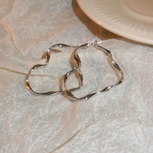 Polished silver irregular wave hoop earrings displayed on elegant beige texture