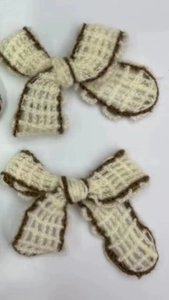 Detail of two beige knitted bow hair clips with brown borders for DIY clothing accessories