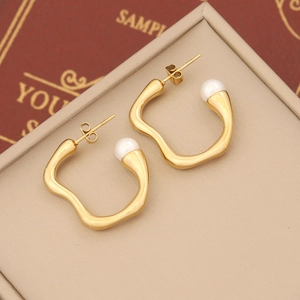 Detail of irregular gold geometric earrings with white pearls on a beige jewelry box