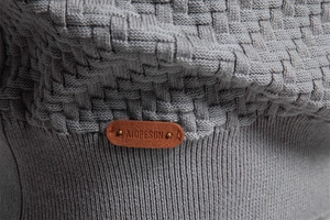 Close-up of grey-blue knit cardigan with refined texture and leather logo detail