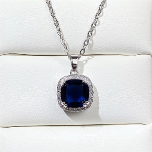 Close-up of square blue crystal necklace with diamond halo on white jewelry box padding