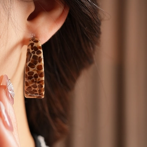 Detail of tortoiseshell acetate C-shaped earrings with leopard pattern on model
