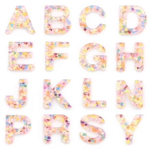 Grid view of 16 resin alphabet charms filled with colorful heart-shaped sequins on white