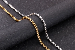 Close-up of gold and silver box chain necklaces showing polished square links on grey surface