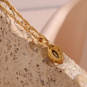 Macro shot of gold marquise pendant on twisted chain over textured stone background