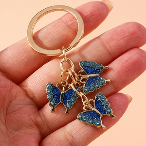 Cute golden keychain with three glitter blue enamel butterflies held in hand for scale