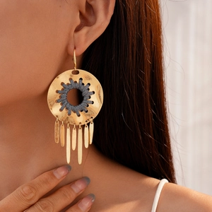 Détail de boucles d'oreilles bohèmes dorées avec tissage gris et breloques à franges