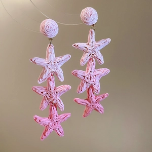 Close-up of pink raffia woven star tassel earrings with handmade braided star pendants