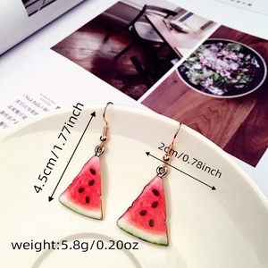 Detail view of handmade watermelon slice drop earrings with red enamel and gold trim
