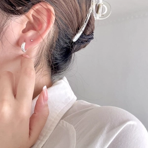 Macro side view of a model wearing minimalist silver twisted hoop earrings and studs