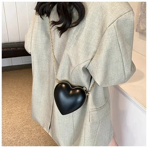 Detail of a chic heart-shaped black crossbody bag with gold chain strap on grey blazer