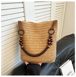 Detail of straw woven bucket bag featuring dark brown leather strap and wooden beads