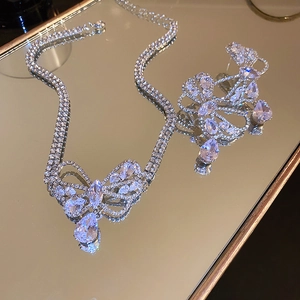 Detail of silver bow and teardrop zircon necklace and earrings on gold mirror