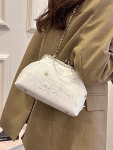 Vintage white floral embroidery kiss-lock bag with silver chain worn by a model