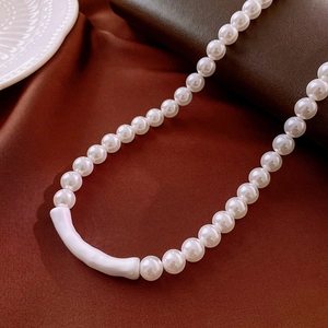 Gros plan d'un collier de perles avec pendentif tube blanc sur soie rouge foncé
