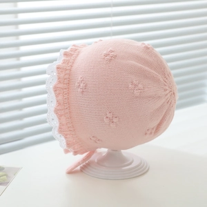 Detail of pink knitted baby hat with white lace trim and pom-pom textured pattern