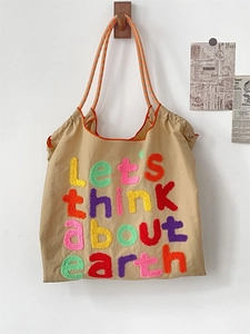 Detail of khaki canvas tote with vibrant rainbow letter embroidery and striped handle