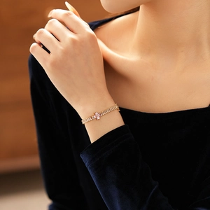 Detail of elegant gold bracelet with zircon stones and pink flower on a model's wrist