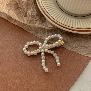 Detail shot of a white pearl bow hair clip with gold metal base on elegant textured background