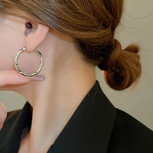 Detail of silver irregular geometric hoop earrings on model with minimalist texture
