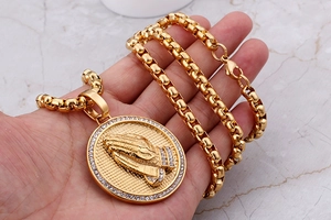 Close-up of golden praying hands pendant with pavé rhinestones and a box chain necklace