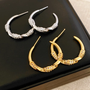 Dettaglio di orecchini a forma di C intrecciata con zirconi placcati oro e argento