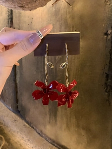 Detail view of red flower drop earrings with golden curved branches and petals