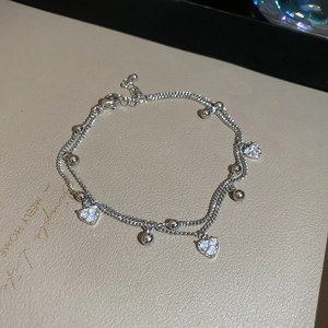 Detail view of double-layer silver bracelet featuring zircon heart charms and round beads