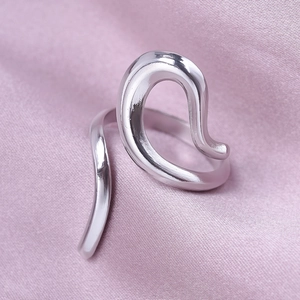 Macro detail of silver geometric wavy open ring on soft purple silk fabric background