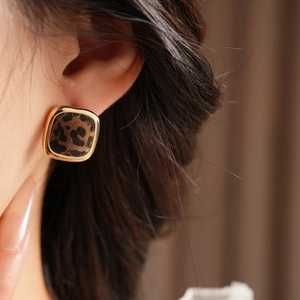 Close-up of square leopard print stud earrings with golden finish on a female model