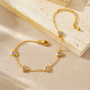 Détail d'un bracelet doré à breloques cœur et pierres violettes sur pierre beige