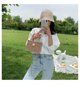 Detail der gewebten Strohbox-Tasche mit Ledergriff und goldener Kettekette auf Gras