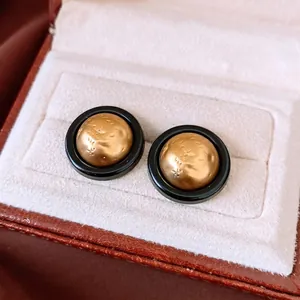Retro round black and gold textured stud earrings displayed on white velvet jewelry box