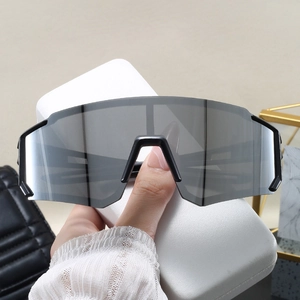 Detail view of large grey shield lens sunglasses held by hand with white travel case